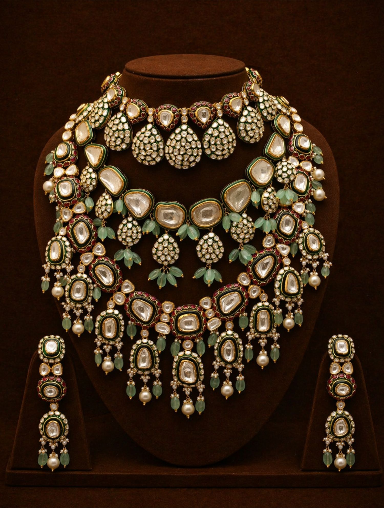 Complete gold kundan jewelry set with choker, multi-strand necklace, and chandelier earrings with diamonds, pearls, and green stones on velvet bust.